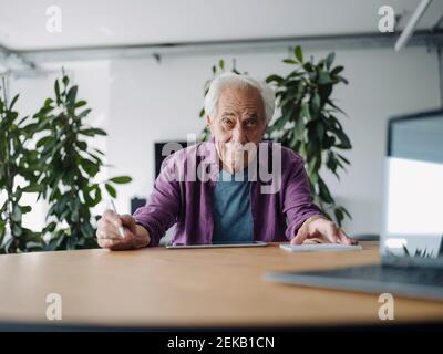 Senior businessman using digital tablet while sitting by table at office Stock Photo