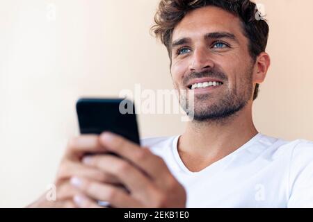 Handsome man smiling while using smart phone at home Stock Photo