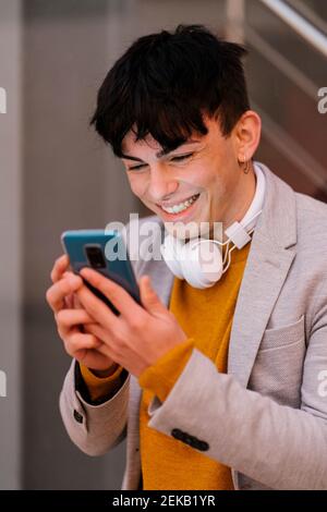 Young man smiling while using mobile phone standing outdoors Stock Photo