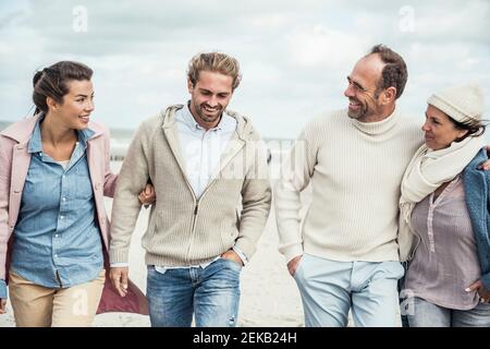 Group of adult friends walking side by side along sandy beach Stock Photo
