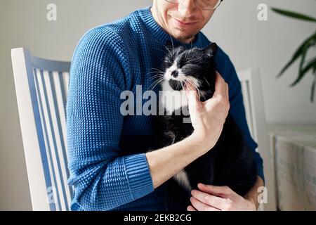 Young man holding his cat in arms during sunny day. Themes trust, care and friendship between people and pets. Stock Photo