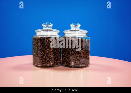 Transparent jars of roasted coffee beans on table against blue background Stock Photo