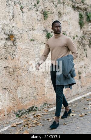 Young man holding jacket while walking on footpath Stock Photo