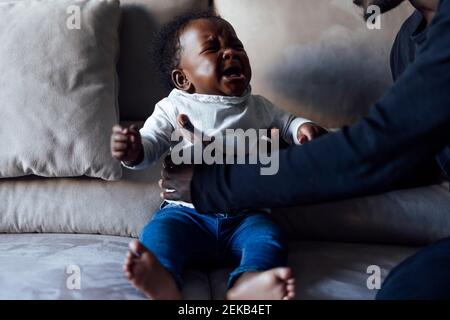 Father lifting crying baby daughter on sofa in living room Stock Photo