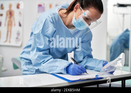 Mature female doctor completing documents related to medical sample in clinic Stock Photo