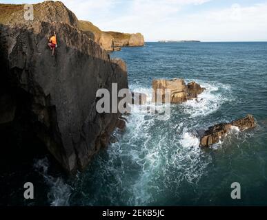 Male rock climber reaching on top of cliff Stock Photo
