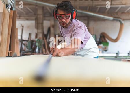 Male carpenter using tape measure while working in workshop Stock Photo