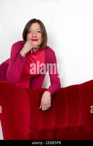 Woman leaning on armchair against white wall Stock Photo