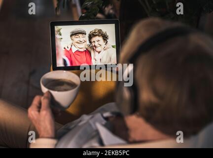Senior woman having video call with couple friends through digital tablet in dark room Stock Photo