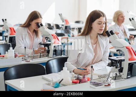 Researchers in white coats working with microscopes in lab Stock Photo