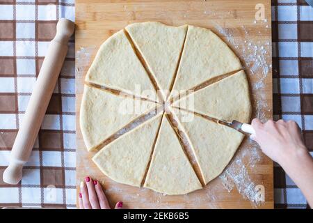 Woman making slices on dough with cutter to make croissants in kitchen Stock Photo