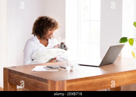 Mother looking at sleeping baby while sitting by table at home office Stock Photo