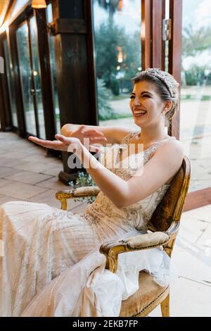 Happy bride clapping hands while sitting on chair at banquet Stock Photo