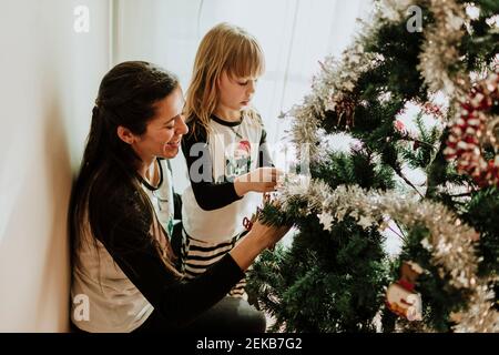 Smiling father carrying girl while holding ornament by Christmas tree Stock Photo