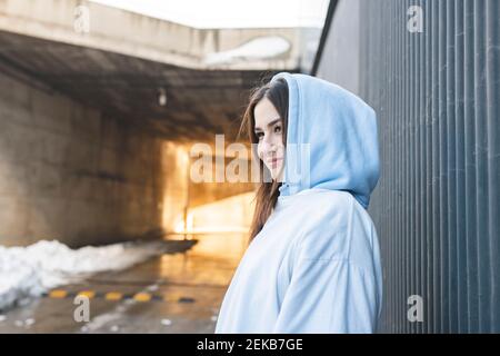 Smiling woman looking away while standing by wall Stock Photo