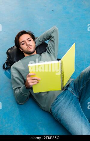 Young man studying while lying on backpack at basketball court Stock Photo