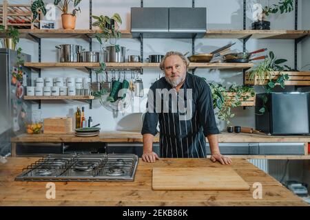 Confident mature chef staring while standing by kitchen counter in kitchen Stock Photo