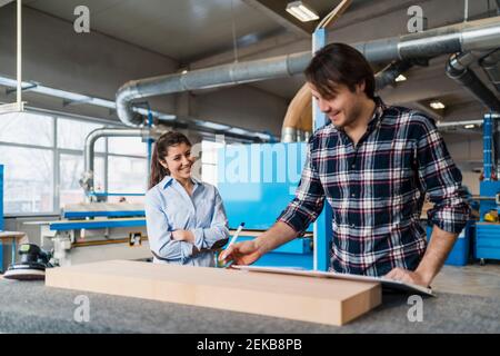 Manual worker measuring wood while standing by colleague at industry Stock Photo