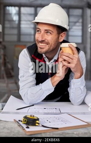 Smiling male architect holding coffee looking away while standing at table Stock Photo