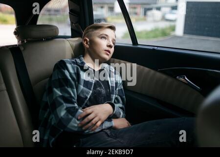 Thoughtful boy looking through window while sitting in back seat of car Stock Photo
