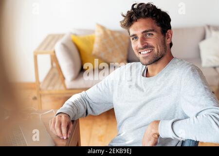 Smiling man looking away while sitting at home Stock Photo