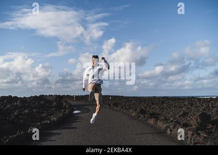 Cheerful male tourist jumping amidst volcanic rock at Los Hervideros on sunny day, Lanzarote, Spain Stock Photo
