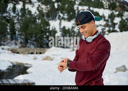 Smiling male athlete checking time in smartwatch while standing on snowfield Stock Photo
