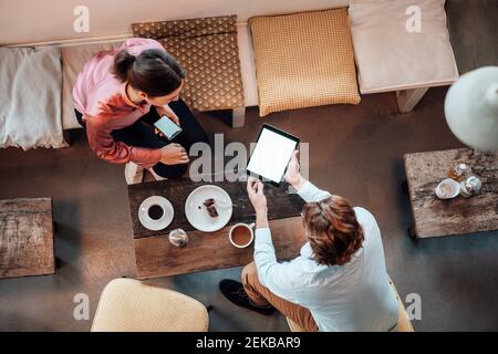 Female and male colleagues discussing over digital tablet at coffee shop Stock Photo