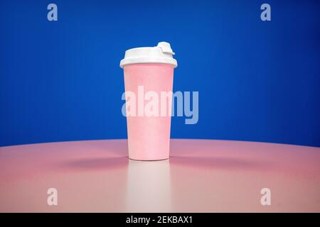 Pink reusable coffee cup on table against blue background Stock Photo