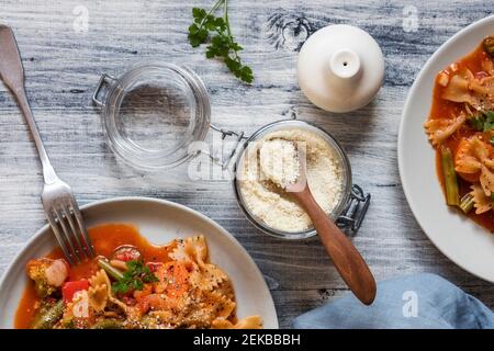 Two plates of vegan pasta with vegetables and jar of shredded vegan Parmesan cheese Stock Photo