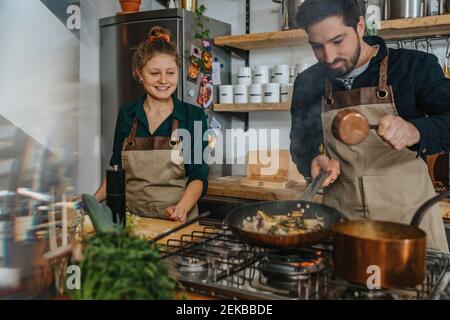 Young chef looking at expertise cooking king oyster mushrooms in frying pan while standing in kitchen Stock Photo