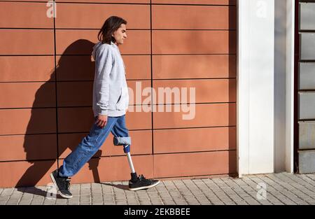 Young man with prosthetic leg walking by wall during sunny day Stock Photo