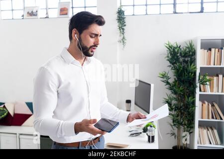 Young male entrepreneur discussing over pie chart through smart phone while working in office Stock Photo