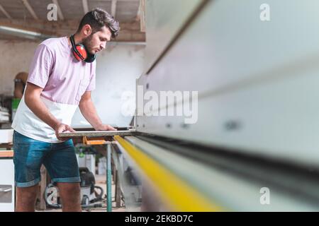 Male craftsperson holding plank while working in workshop Stock Photo