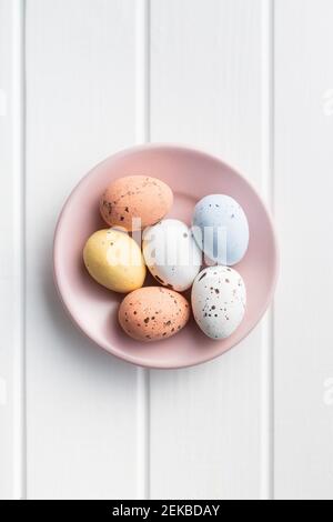 Chocolate easter eggs. Sweet candy eggs on pink plate on white table. Top view. Stock Photo