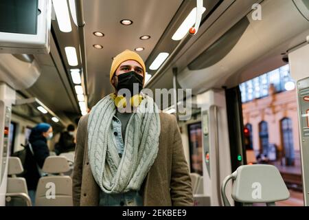 Man wearing protective face mask looking away while standing in train Stock Photo
