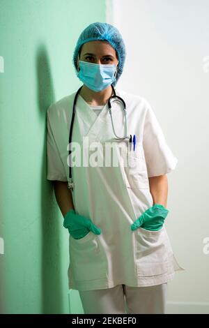 Female doctor with hands in pockets leaning by wall at clinic Stock Photo
