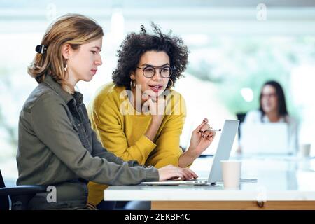 Female colleagues planning strategy while discussing over laptop at desk in office Stock Photo