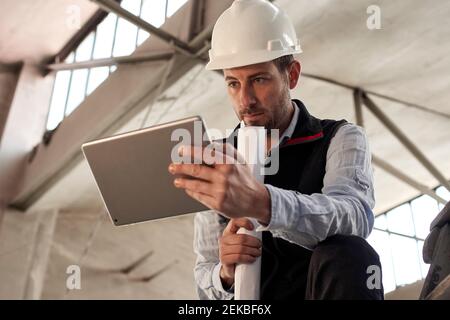 Serious male engineer using digital tablet while standing in building at site Stock Photo