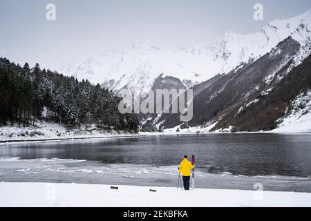 Man with ski at snow covered lakeshore in front of mountains Stock Photo