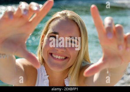 Cheerful young woman showing finger frame while standing against lakeshore on sunny day Stock Photo
