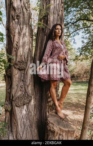Mature woman wearing traditional clothing looking away while leaning on tree Stock Photo