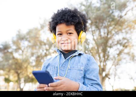 Smiling boy with headphones using mobile phone while standing at park Stock Photo