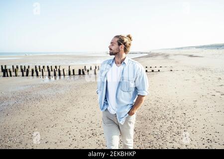 Handsome man with hands in pockets standing at beach on sunny day Stock Photo