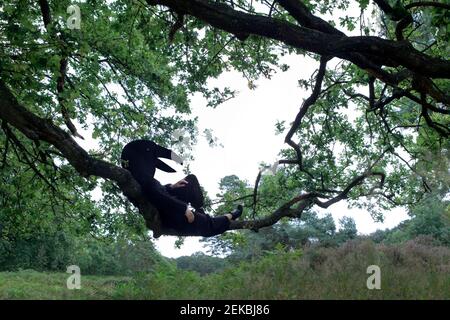 Woman in bird costume lying on tree branch Stock Photo