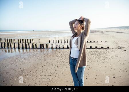 Beautiful woman contemplating while standing on sand at beach Stock Photo