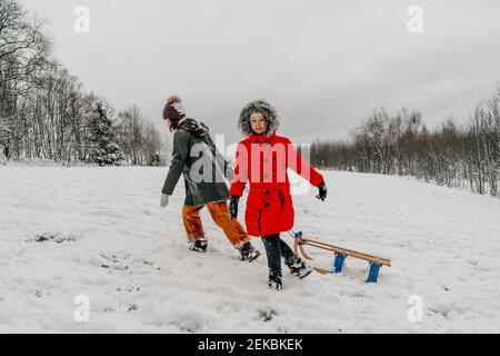 Teenage girl pulling sled while small girl walking on snow during winter Stock Photo