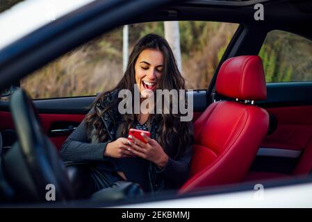 Excited woman using mobile phone while sitting in car Stock Photo