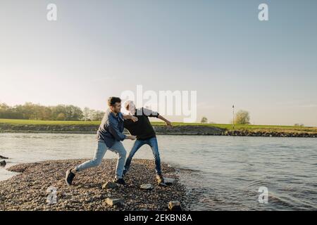 Father and son throwing pebbles in river against clear sky during autumn Stock Photo