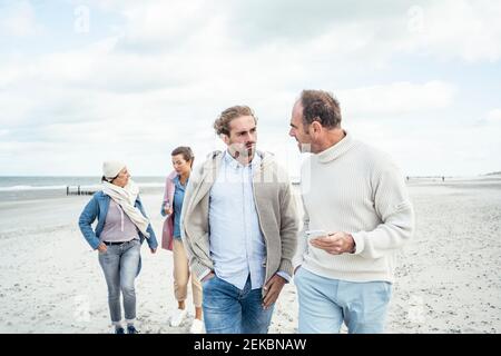 Two men walking and talking side by side along sandy beach Stock Photo